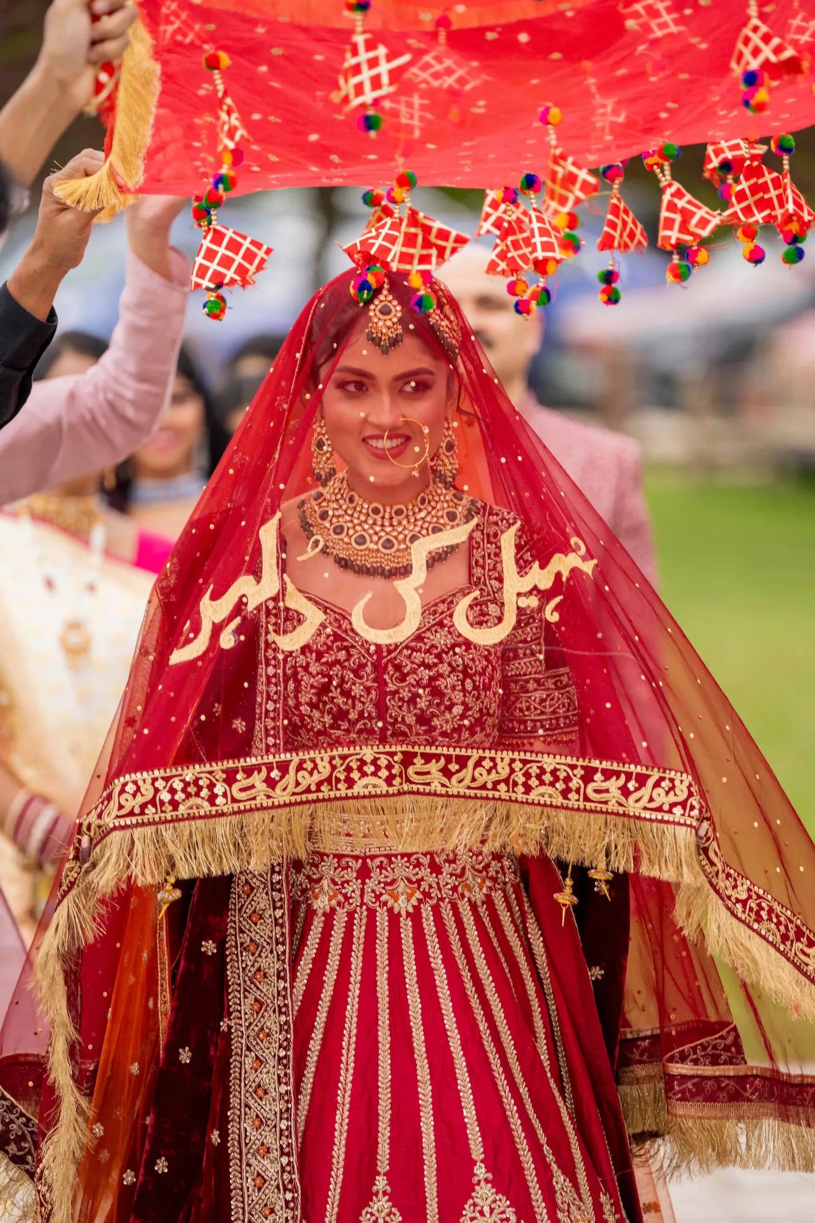 Bride beneath the canopy, her gold-lettered dupatta framing her face