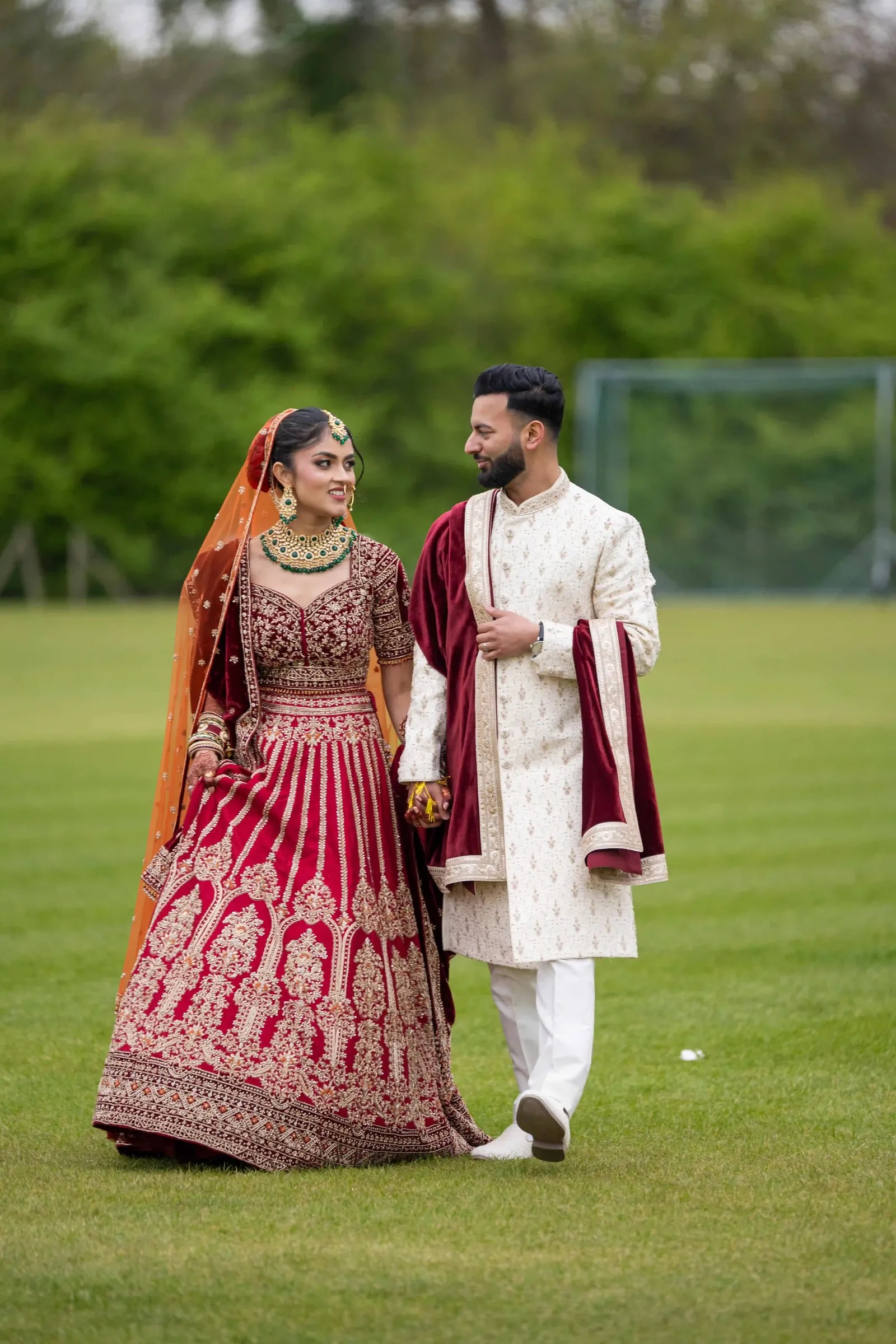 Couple walking together on the grass, both in deep red and ivory