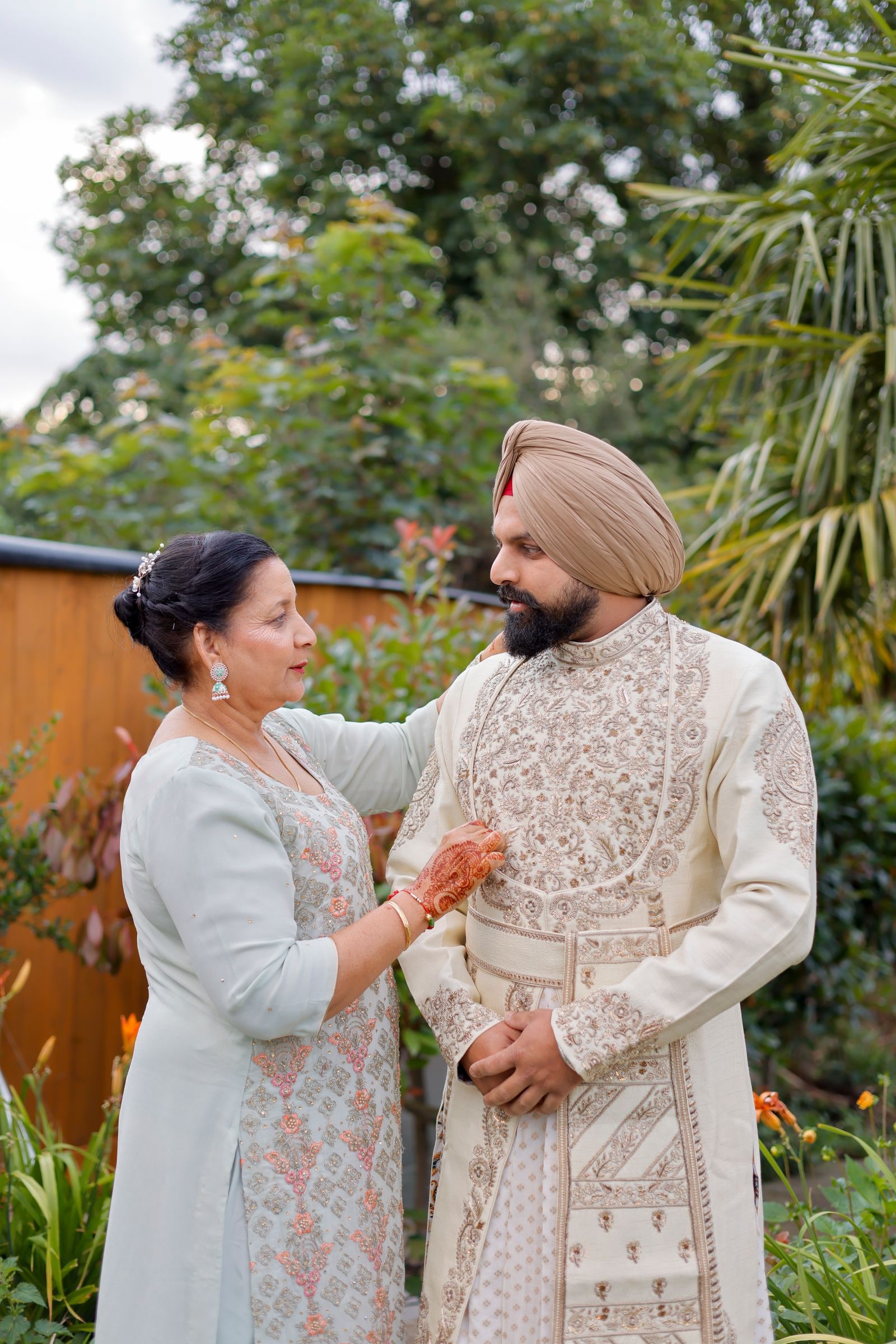 The groom's mother straightening his sherwani in the garden