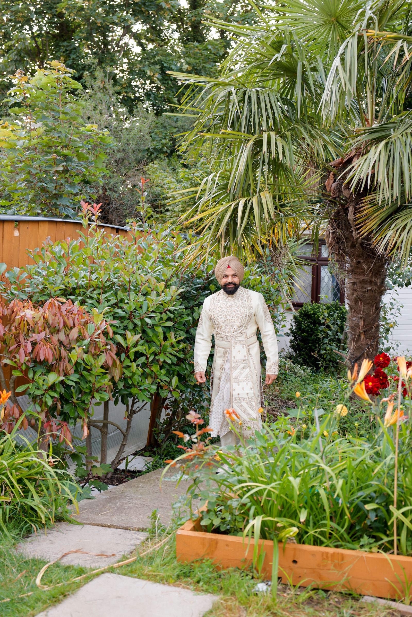 Groom walking up the garden path in an ivory sherwani and turban