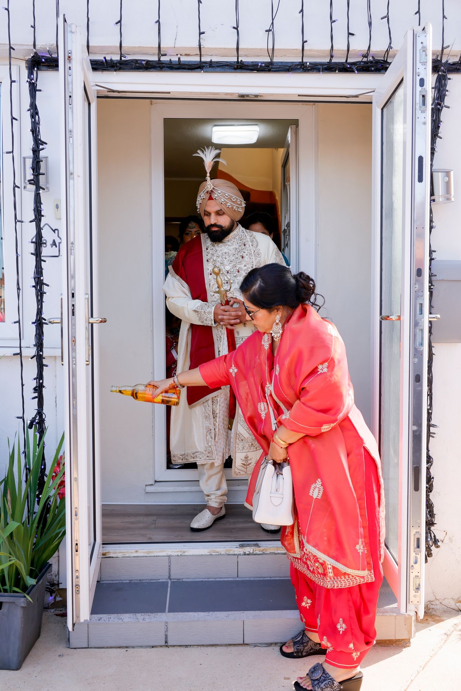 A relative in red performing a blessing at the doorway as the groom leaves the house