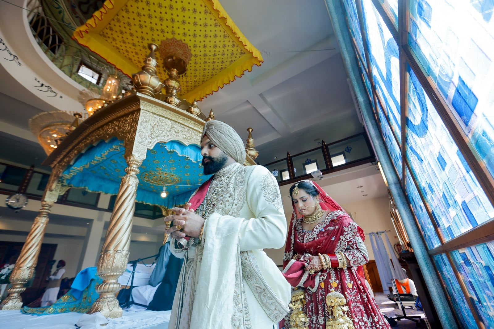 Bride and groom standing before the palki, her red lehenga heavy with gold