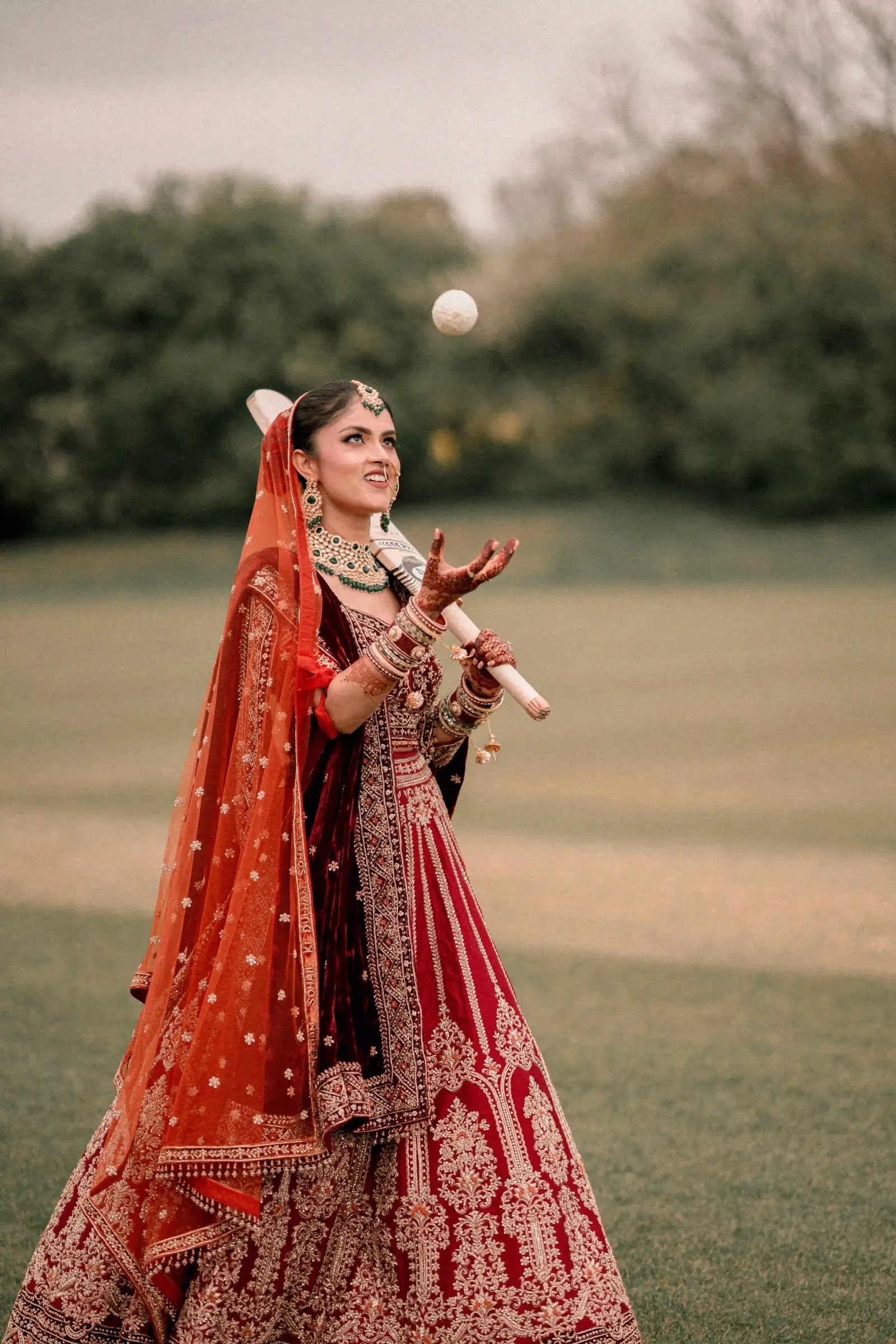 Bride tossing the cricket ball up in front of her, bat held under her arm