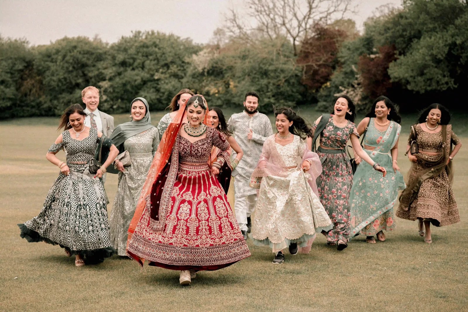 Bride running across the grass with her friends in a line behind her