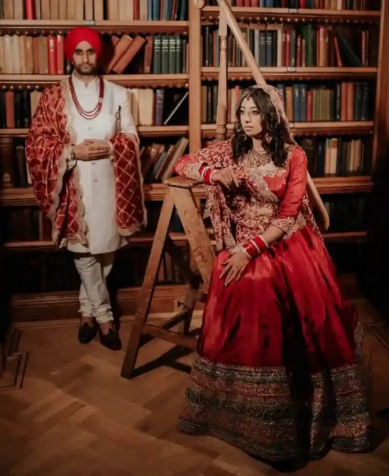 Groom on a library ladder above his bride, who sits below in a red lehenga