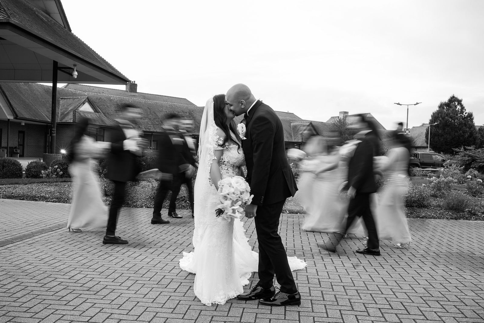 Groom dipping his bride as guests blur past them, in black and white