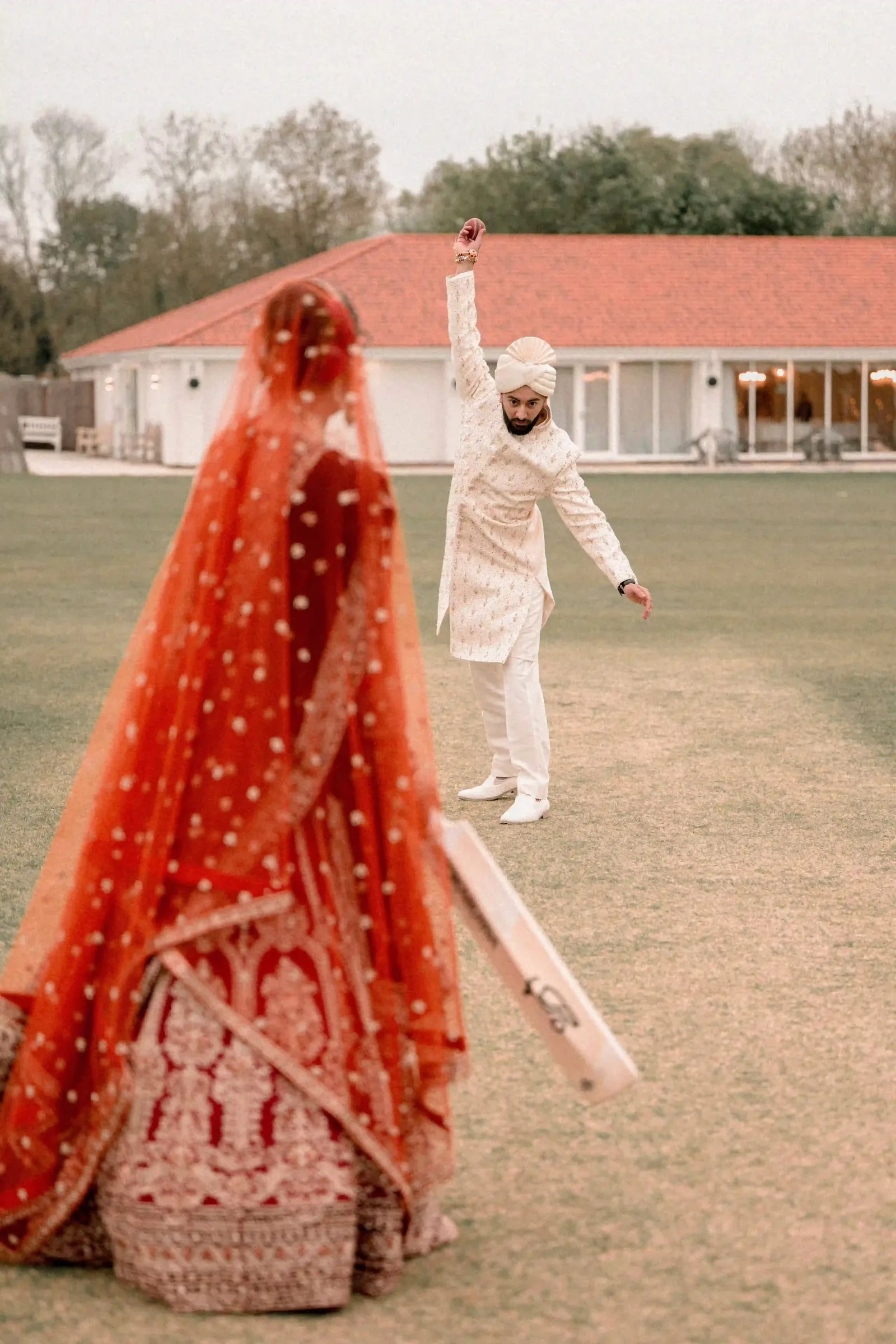 Groom celebrating with his arm up after bowling his bride out, bat still in her hand