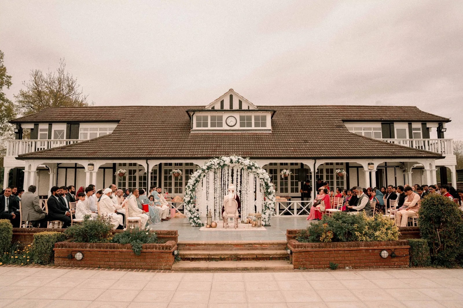 The ceremony set out on the pavilion terrace, guests seated around a white flower arch