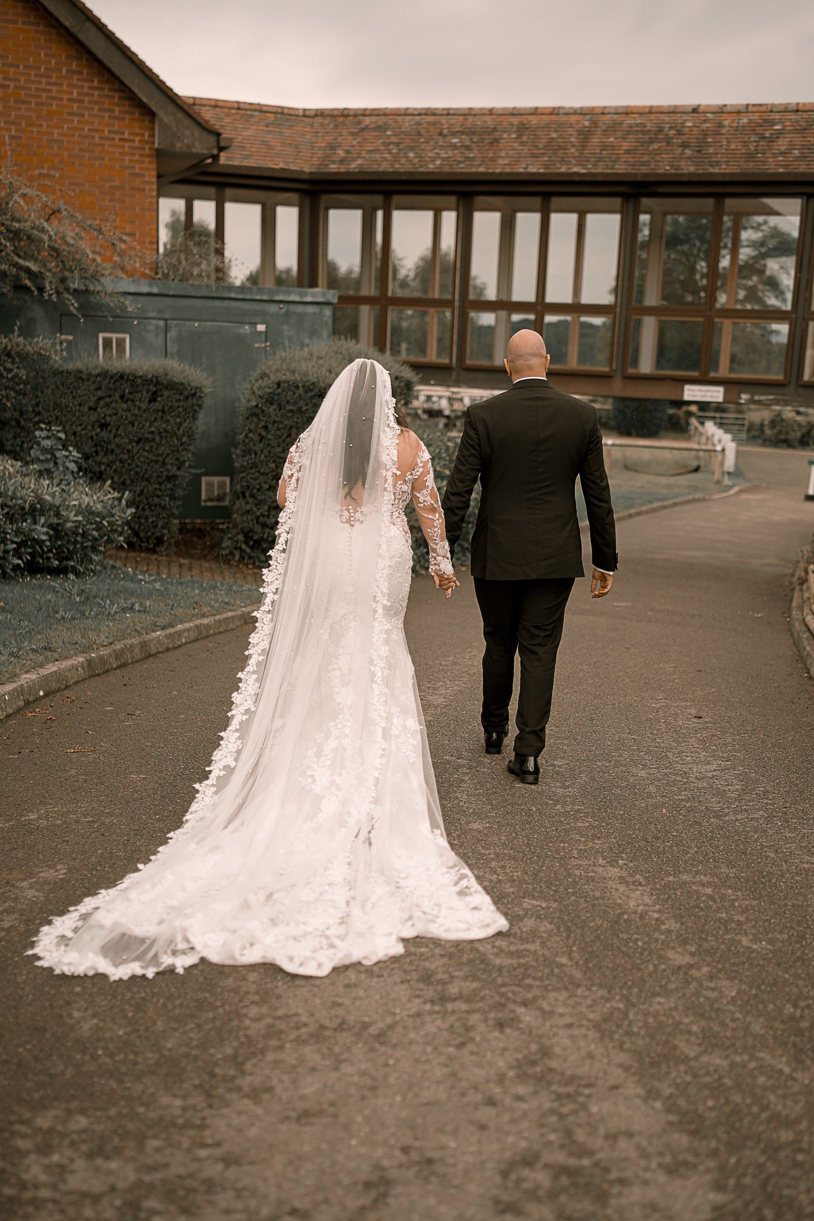 Bride and groom walking away up the path, her lace train trailing behind her