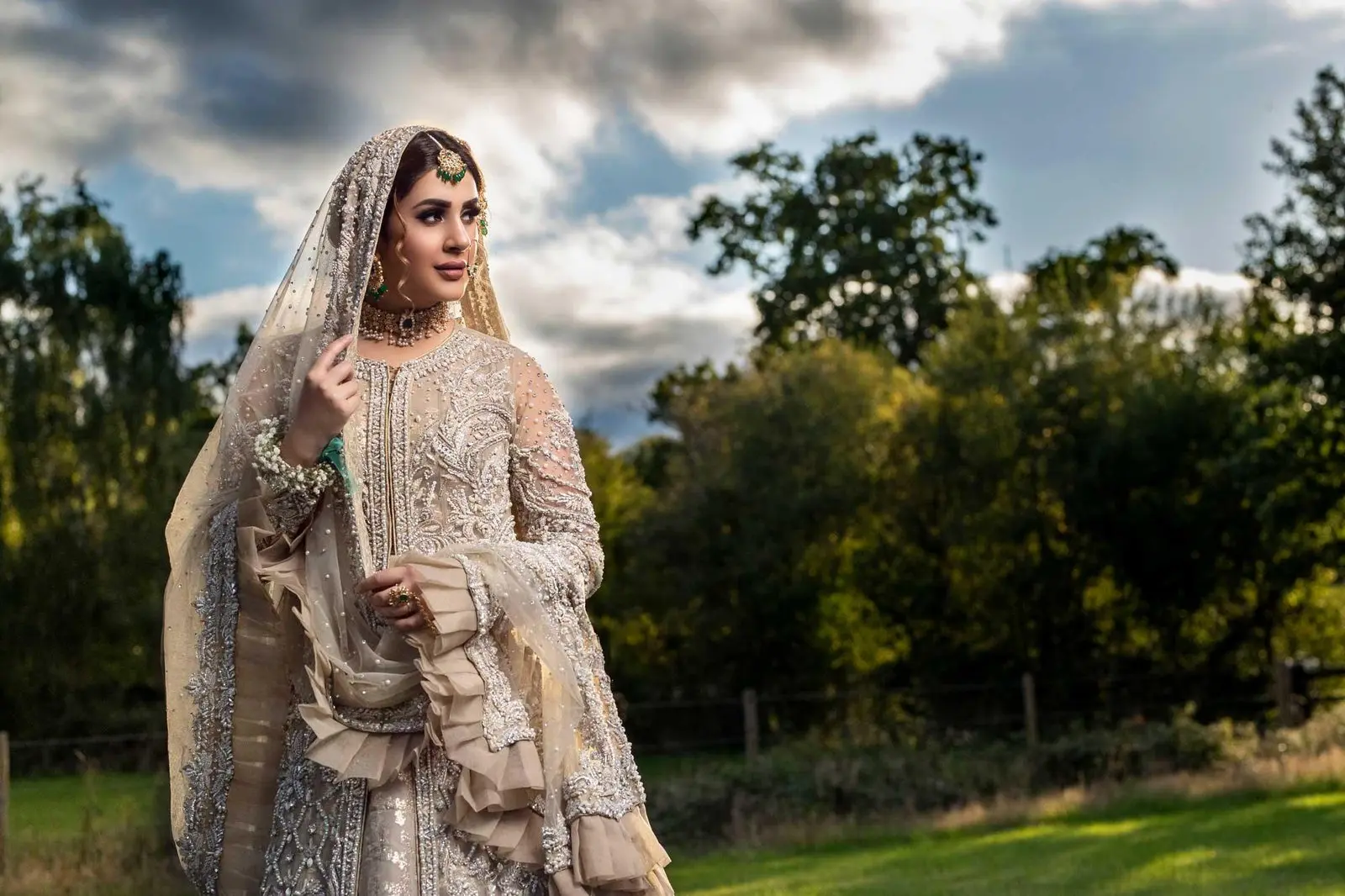 Bride in cream and gold embroidered bridal wear with veil, outdoors — Asian wedding photography by Memory Filming, London