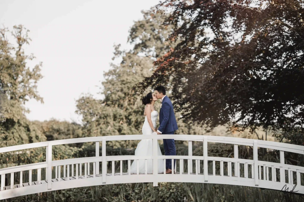Bride and groom sharing a kiss on a white footbridge surrounded by trees, London wedding photography