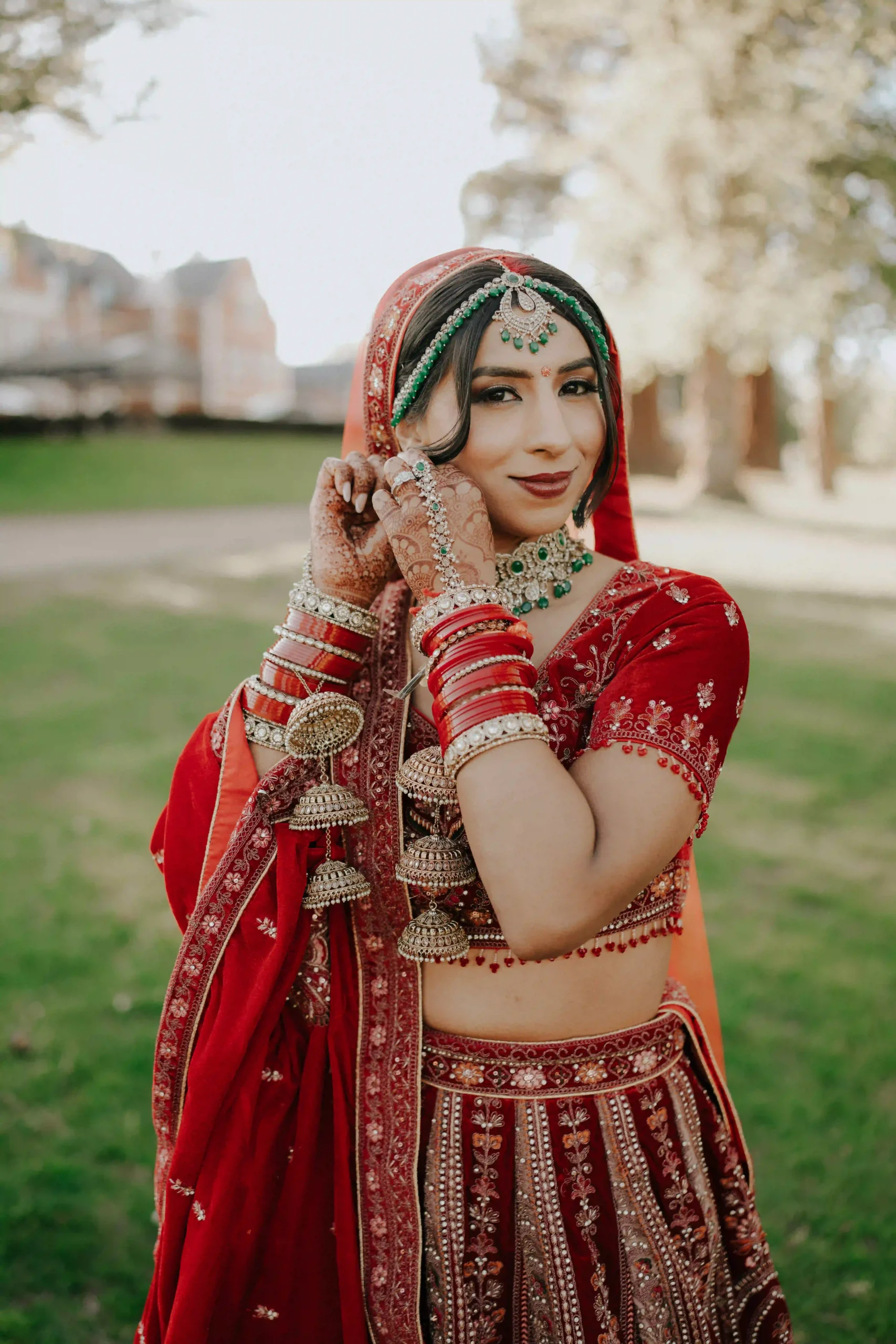 Close-up photo of Hindu bride in red velvet lehenga with green and gold bridal jewellery