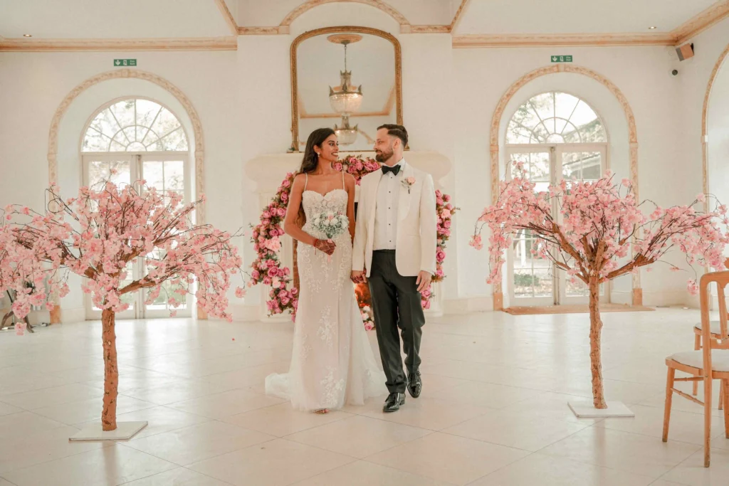 Hindu bride and groom walking hand in hand past cherry blossom trees at wedding reception, London