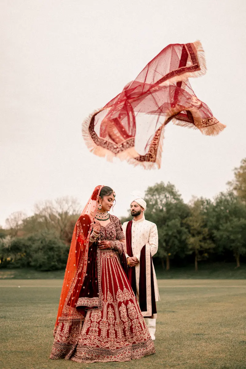 South Asian bride and groom portrait with red dupatta flying in the air, multicultural wedding photography in London