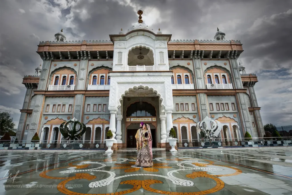 Sikh bride and groom in traditional attire outside an ornate gurdwara, captured by a Sikh wedding photographer in London