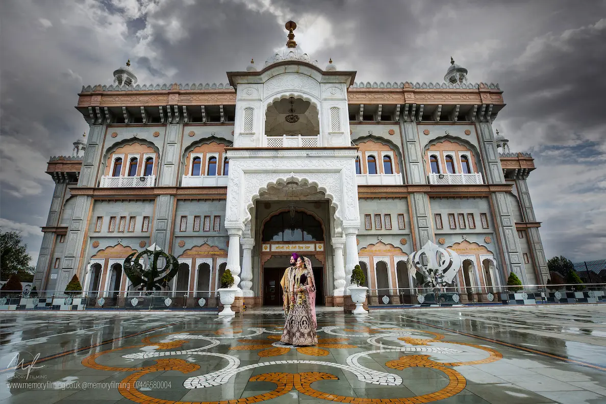 Sikh bride and groom in traditional attire outside an ornate gurdwara, captured by a Sikh wedding photographer in London