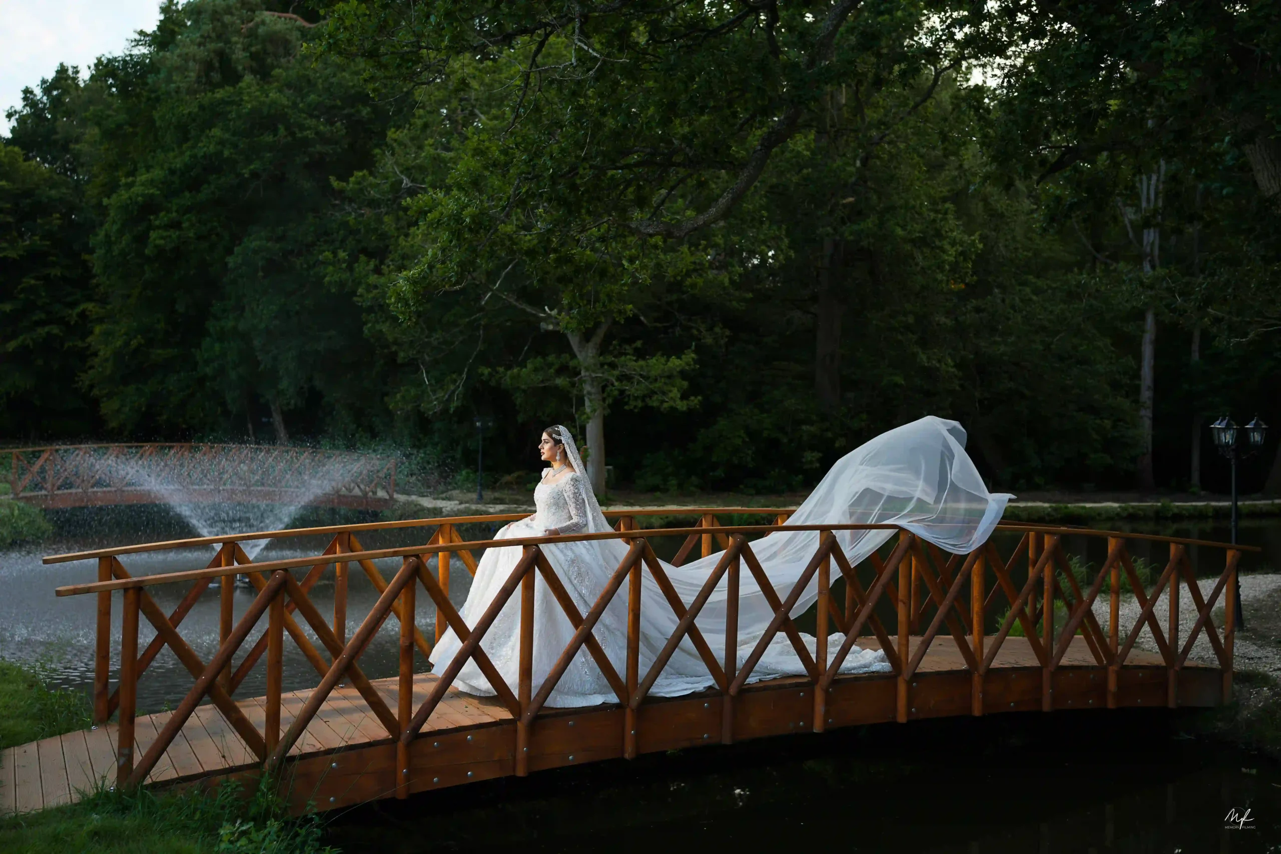 Bride in a white gown with a flowing long veil on a wooden estate bridge photographed by a London Asian wedding photographer