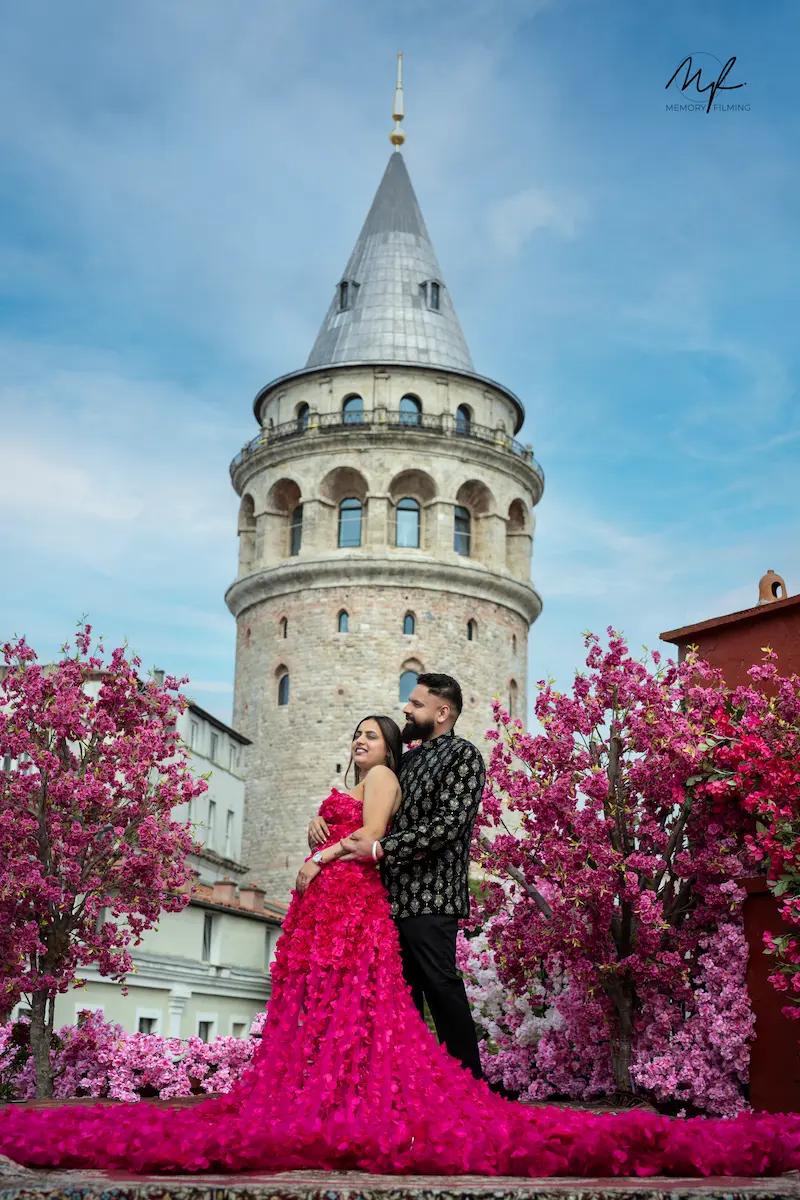 Bride in a vibrant pink gown embracing her groom in front of Galata Tower and pink blossoms in Istanbul Turkey