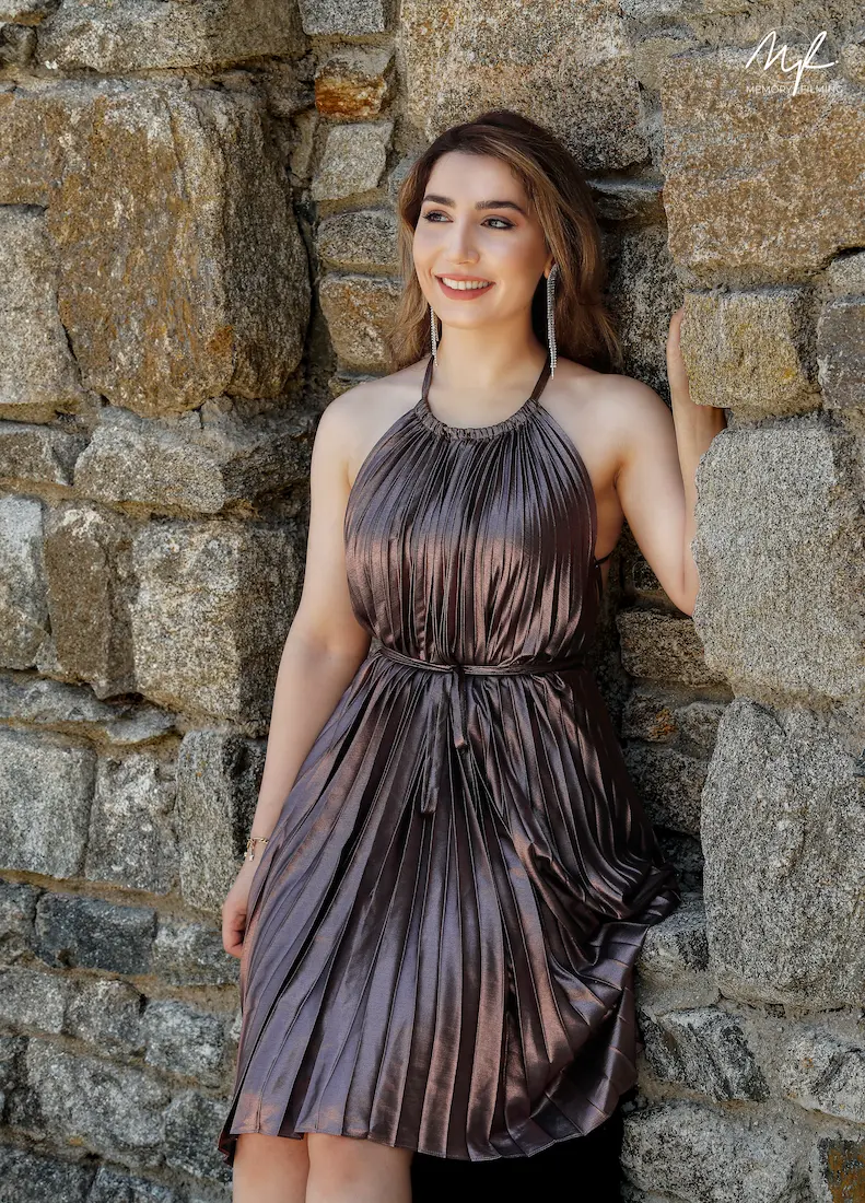Smiling bride wearing a pleated halter gown leaning against an ancient rustic stone wall during a destination photo session
