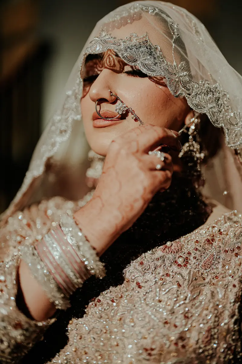 Bride in a dark red outfit standing in front of her groom on a decorated stage with pink and white floral arches and chandeliers