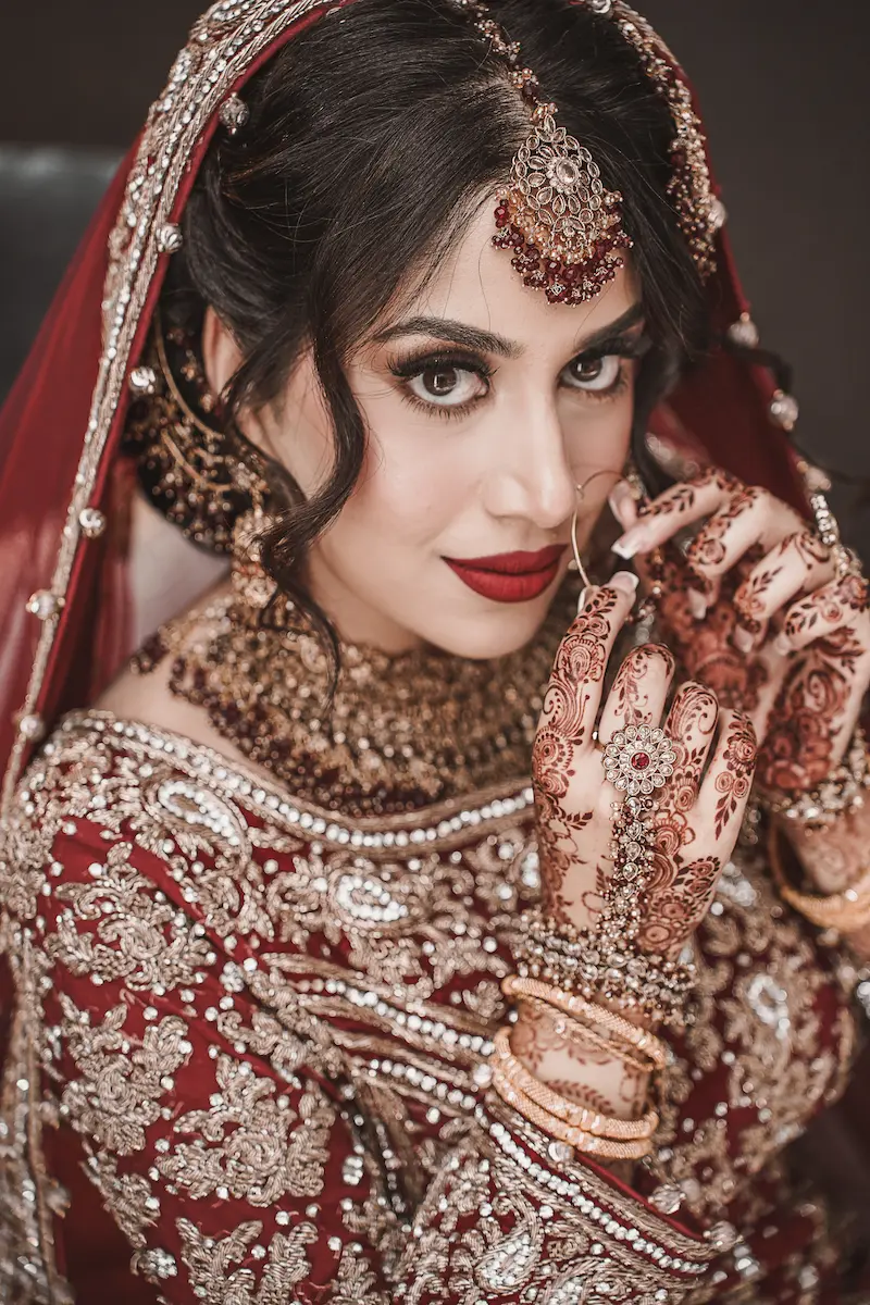 Extreme close-up portrait of a bride displaying detailed bridal makeup, nose ring, stone necklace, and intricate henna mehndi designs